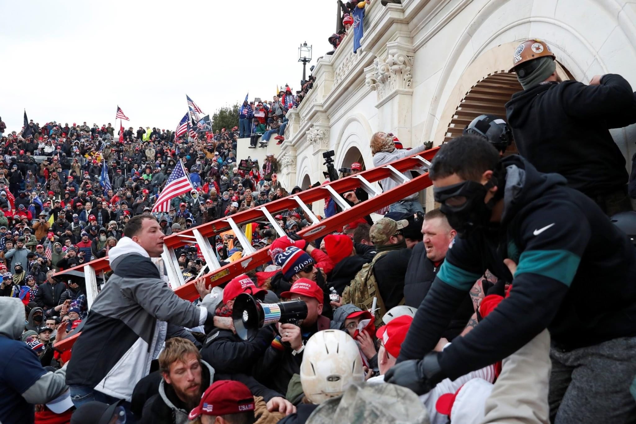 Insurrectionists swarm the Capitol steps in Washington D.C. on January 6. One is holding a ladder to breach the Capitol building.
