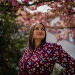 Photo of Ruchika Tulshyan. She is wearing a maroon floral shirt standing in front of cherry trees.