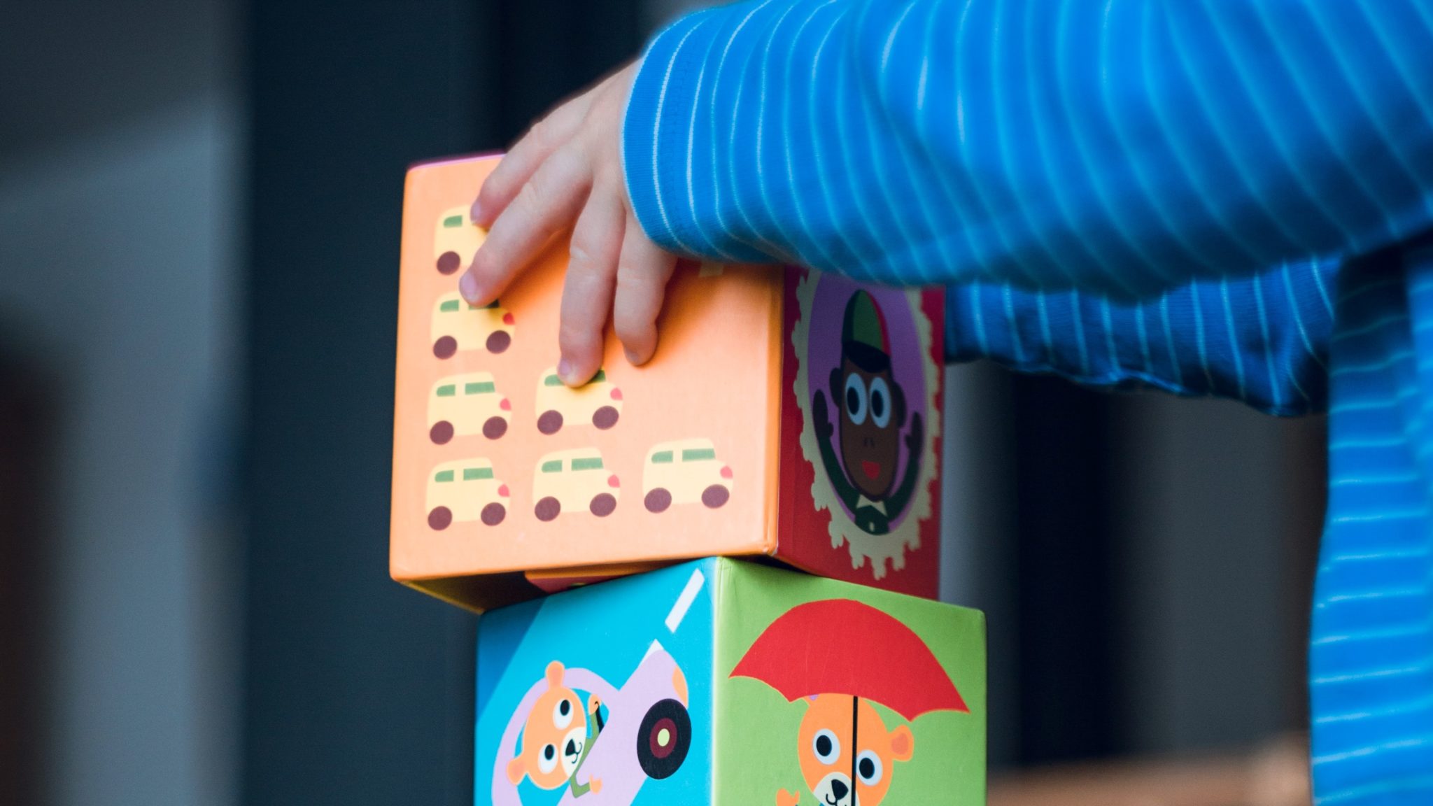 Building blocks with illustrated images on them. A child's hands are stacking them on top of each other.