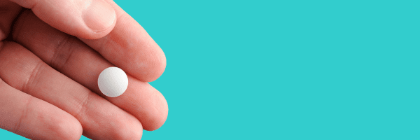 A hand holding a small, round, white pill.