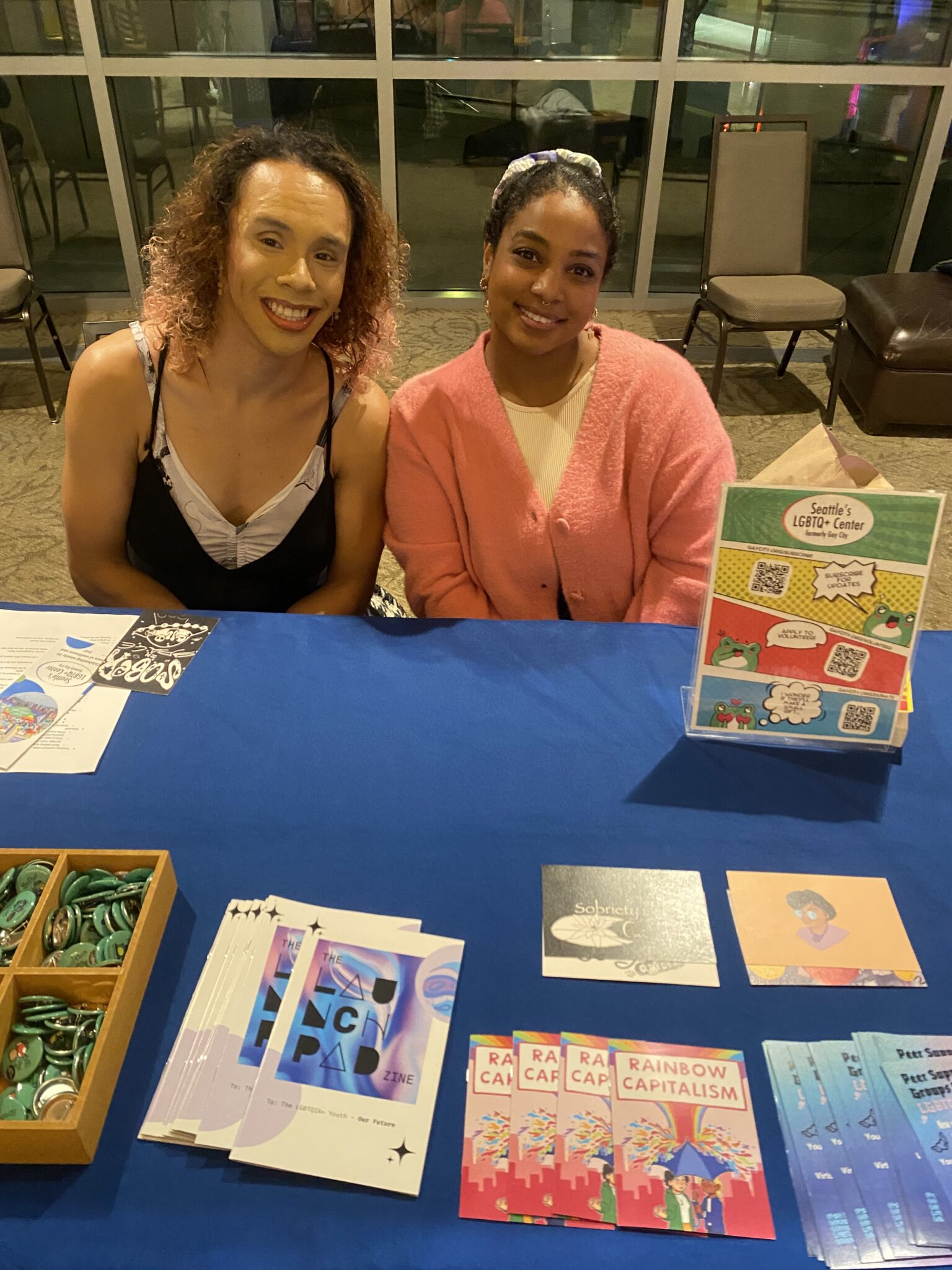 Two people smiling behind a table with brochures on it.